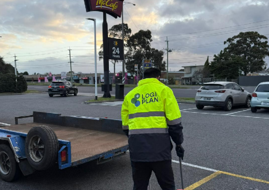 A LogiPlan grounds crew member sweeping and clearing a commercial car park at dawn